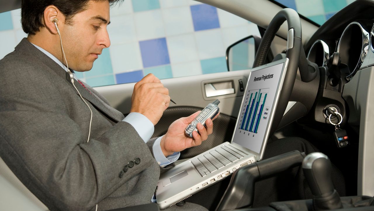 Businessman using his laptop computer and PDA in his car --- Image by © Steve Hix/Somos Images/Corbis