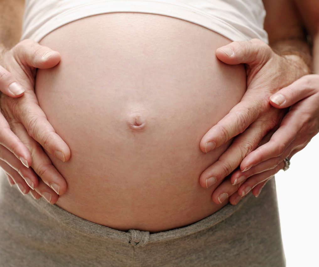 Expectant parents. Pregnant woman and her partner resting their hands on her swollen abdomen. She is in her third trimester. --- Image by © Ian Hooton/Science Photo Library/Corbis