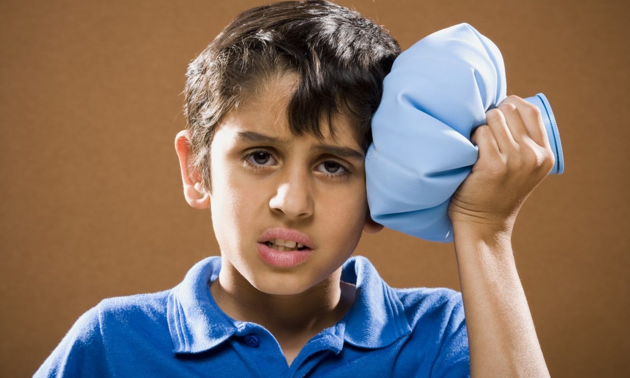Boy holding ice pack to head --- Image by © Mike Kemp/Rubberball/Corbis
