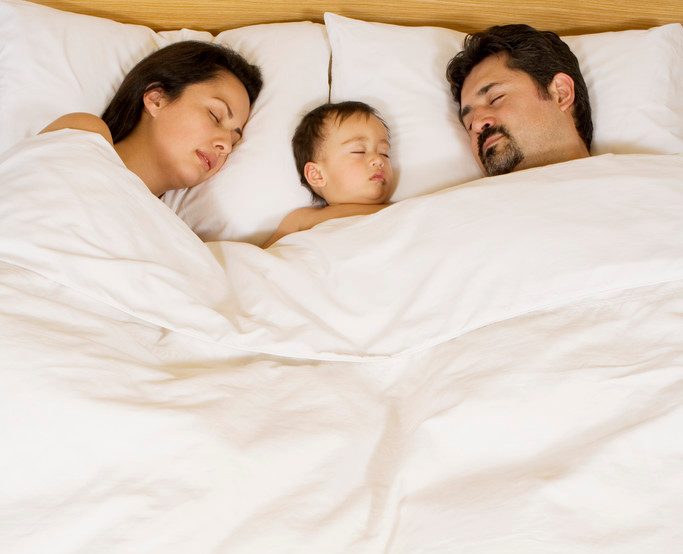 Parents Lying with Infant in Bed --- Image by © MM Productions/Corbis