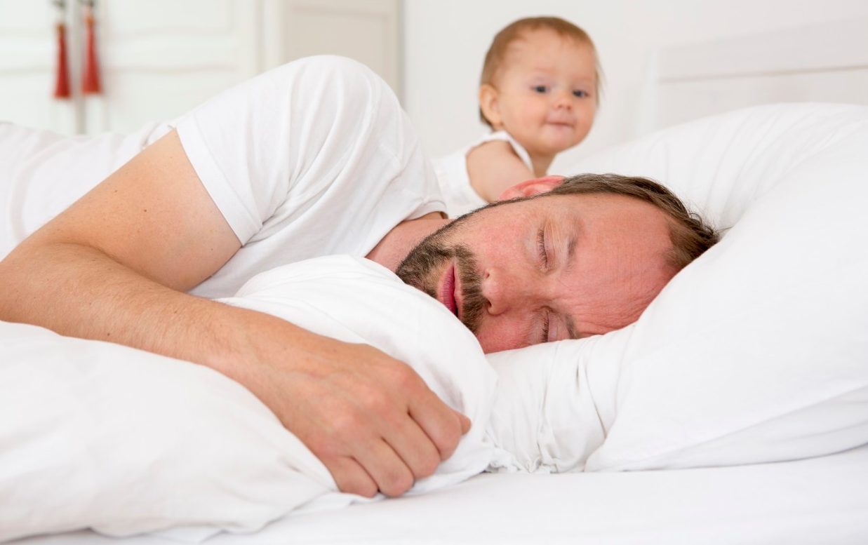 13 Jul 2014 --- Father asleep in bed, baby daughter watching --- Image by © Judith Haeusler/Corbis