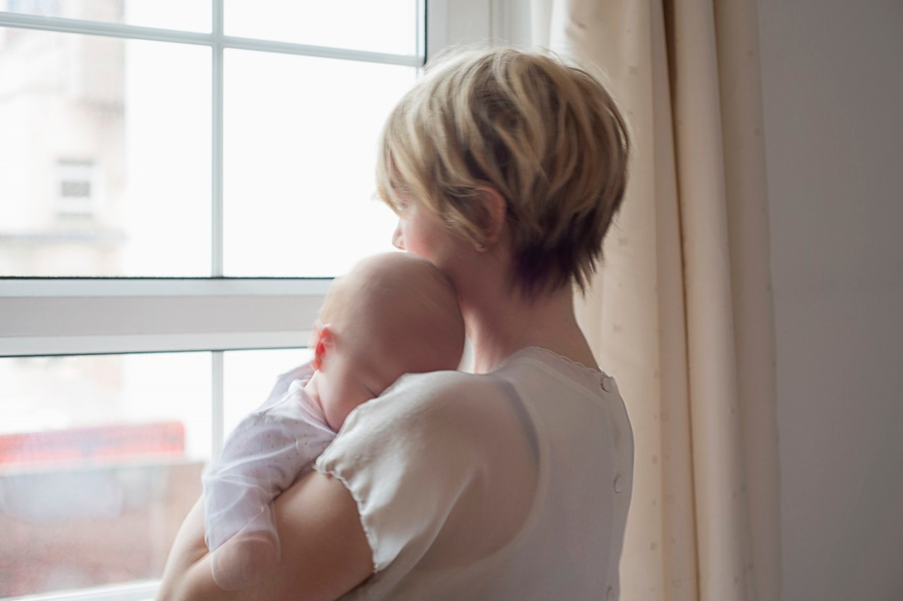 25 Nov 2014 --- Mother carrying sleeping baby girl, looking out window --- Image by © Cecilia Cartner/Corbis