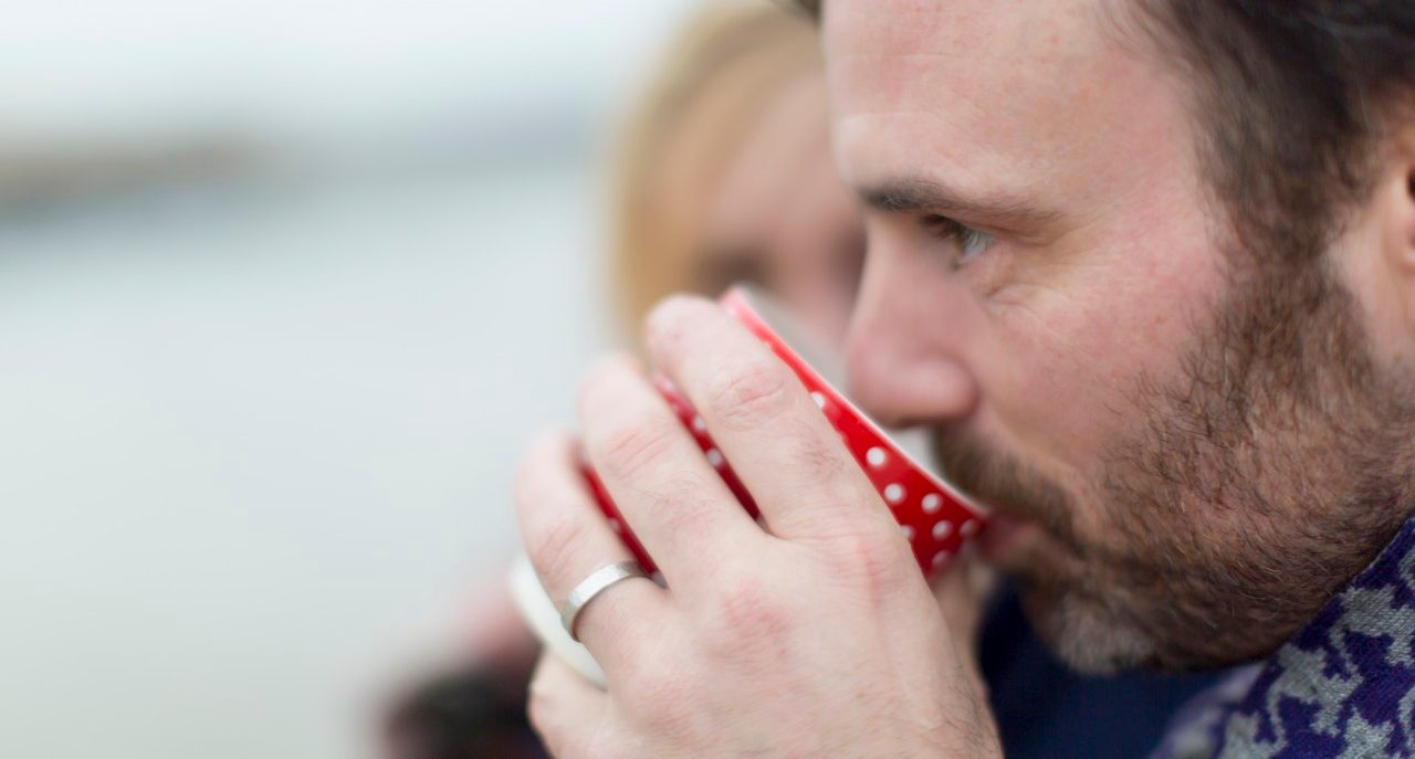 16 Nov 2014 --- Couple on beach, man drinking hot drink --- Image by © dotdotred/Corbis
