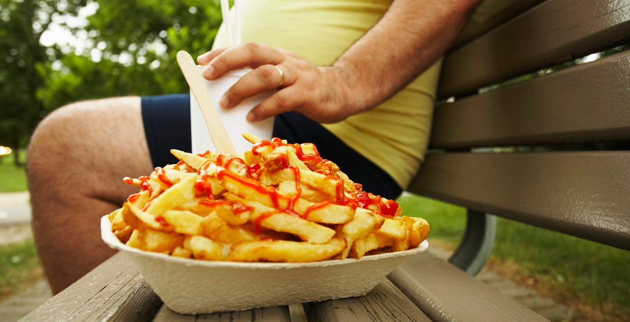 Overweight Man on Bench Next to French Fries --- Image by © Peter Reali/Corbis