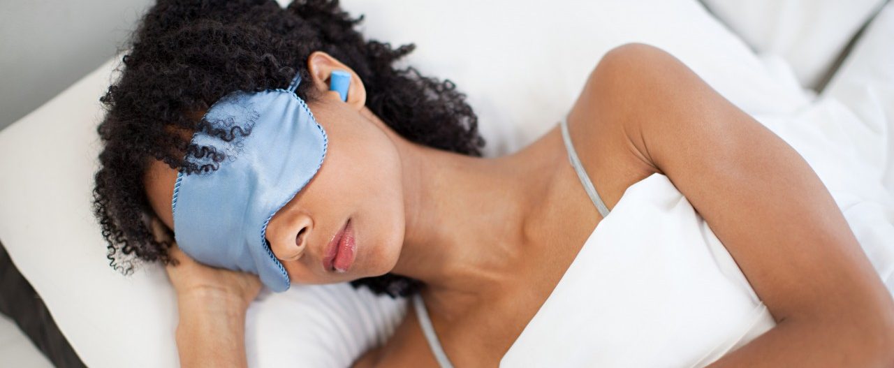 Woman sleeping in eye mask and ear plugs --- Image by © Image Source/Corbis