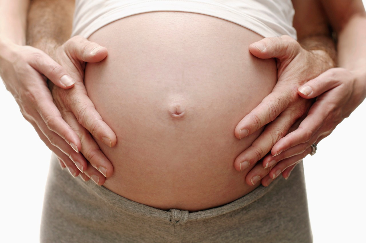 Expectant parents. Pregnant woman and her partner resting their hands on her swollen abdomen. She is in her third trimester. --- Image by © Ian Hooton/Science Photo Library/Corbis